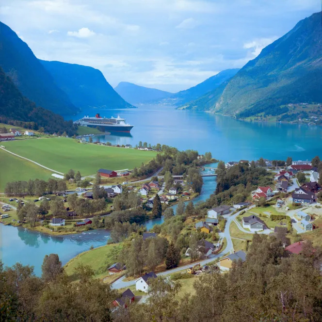Cruise ship on a blue fjord with mountains, fields, and a village