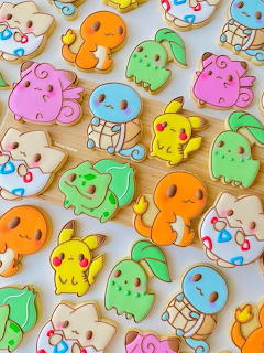 Assorted frosted cookies shaped like Pokémon characters in pink, yellow, orange, blue, and green colors