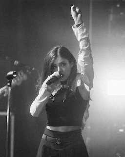 Black-and-white photo of a female singer on stage holding a microphone with one arm raised.