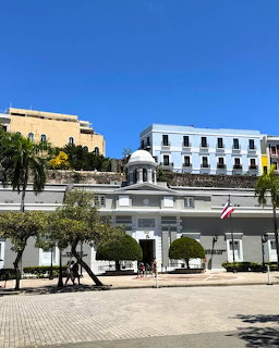Colonial white buildings with a domed entrance and trees in a sunny plaza in Puerto Rico