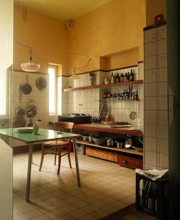Vintage kitchen with yellow walls, white tiles, green table, red chairs, and open shelving with cookware
