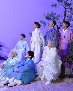 BTS members in white robes in purple-lit studio with pine branches