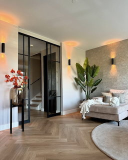 Modern living room with chevron wood floor, beige sofa, plant, and black framed glass doors