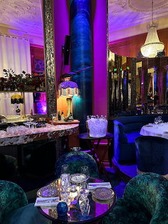 Upscale restaurant dining room with purple-lit decorative columns, crystal chandeliers, and formal table settings