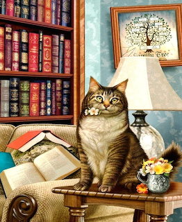 Tabby cat on desk with lamp, books, and framed tree artwork in cozy library setting