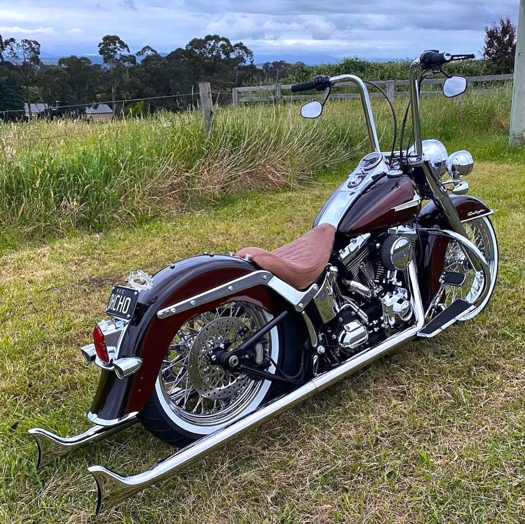 Burgundy Harley-Davidson motorcycle parked on gravel in grassy field with trees in background