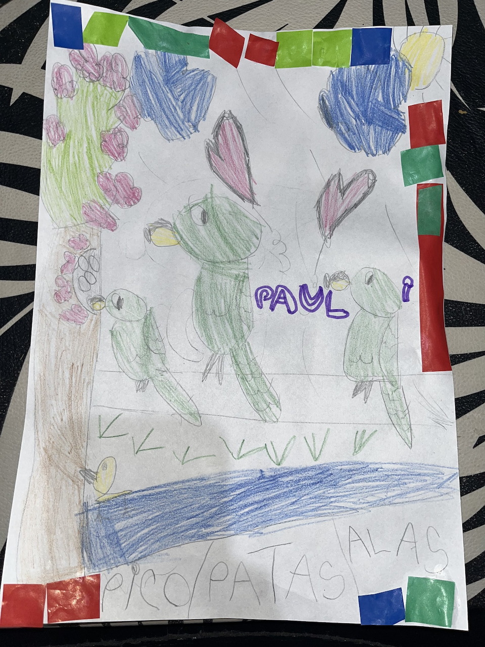 Child's crayon drawing with green birds, pink hearts, a tree, and the name Paul written in purple