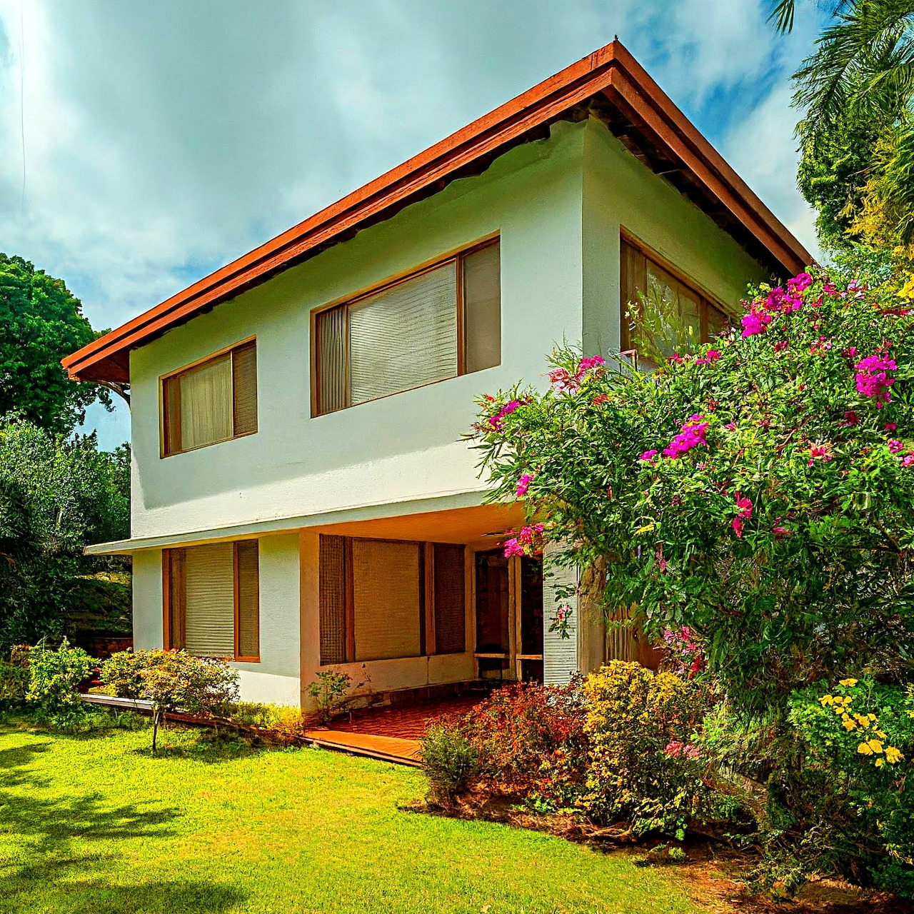 Modern white house with red roof and tropical garden landscaping under blue sky