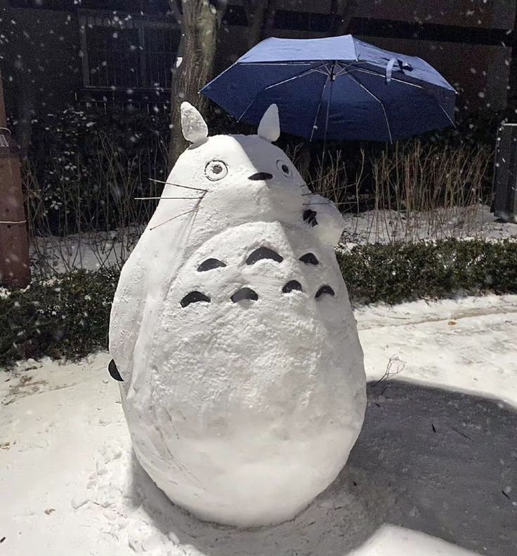 Snow sculpture of Totoro holding blue umbrella in winter scene