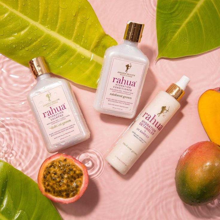 Rahua shampoo and conditioner bottles arranged with tropical leaves, mango, and passion fruit on pink background