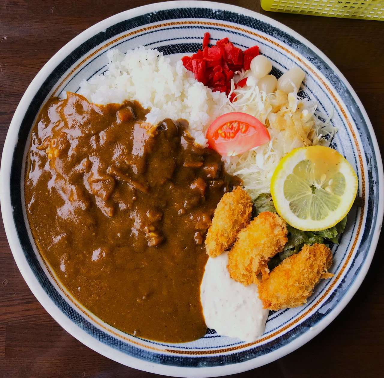 Plate of Japanese curry rice with fried seafood, egg, lemon, cabbage, and pickles