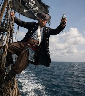 Pirate in period costume climbing ship rigging over the sea with a black pirate flag behind him