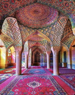 Ornate pink mosque interior with detailed geometric tile patterns, twisted columns, arches and colorful Persian rug