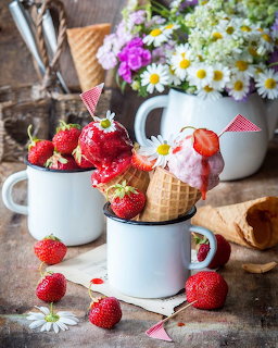 Strawberries in white enamel mugs with daisies and waffle cones on rustic wood table
