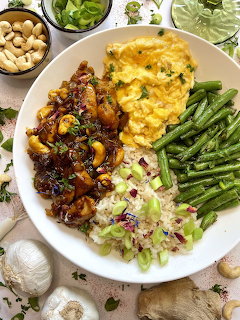 Overhead view of a colorful chicken rice bowl with vegetables, eggs, and Asian-style glazed chicken on a white plate