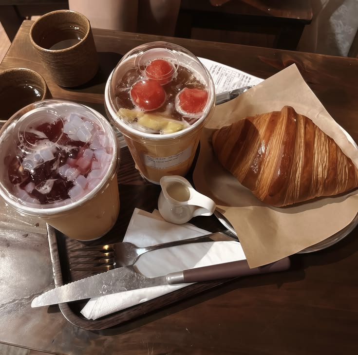 Tray with two iced coffee drinks, a croissant, and utensils on a wooden table
