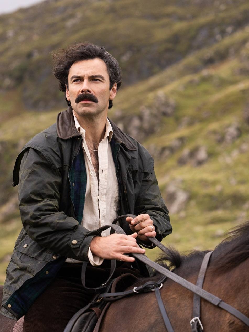 Man in 18th century costume with mustache on horseback in hilly countryside