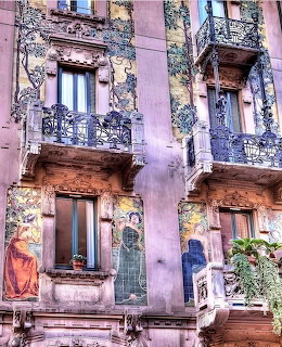 Aged pink building with ornate balconies, painted murals, and traditional shuttered windows