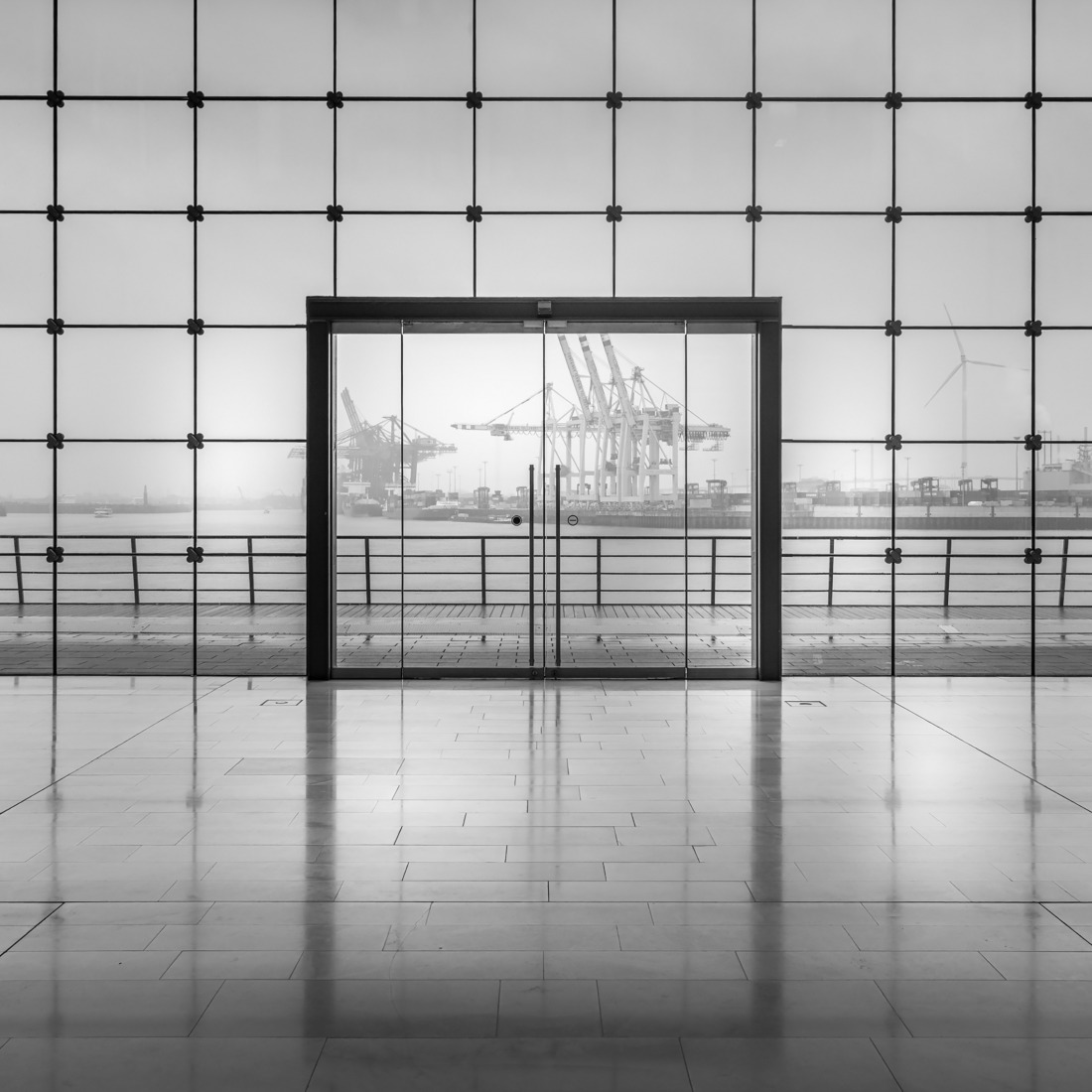 Monochrome interior with glass wall and doorway overlooking harbor cranes