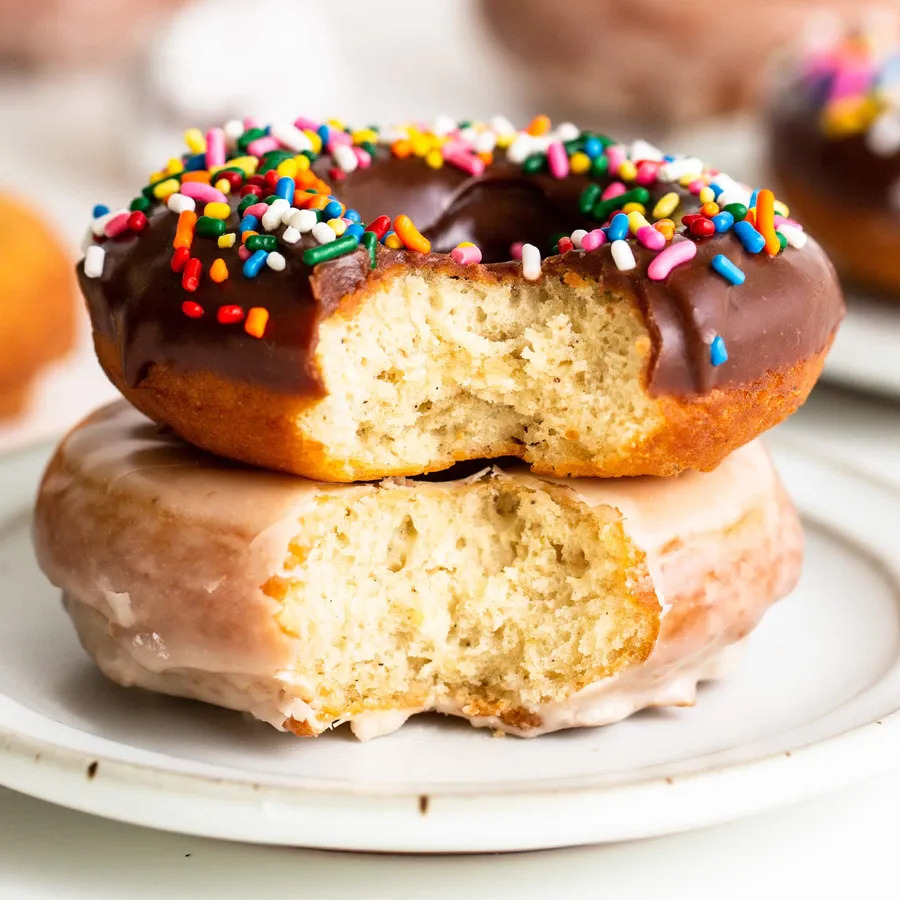 Two bitten donuts on a white plate, one chocolate sprinkled and one glazed