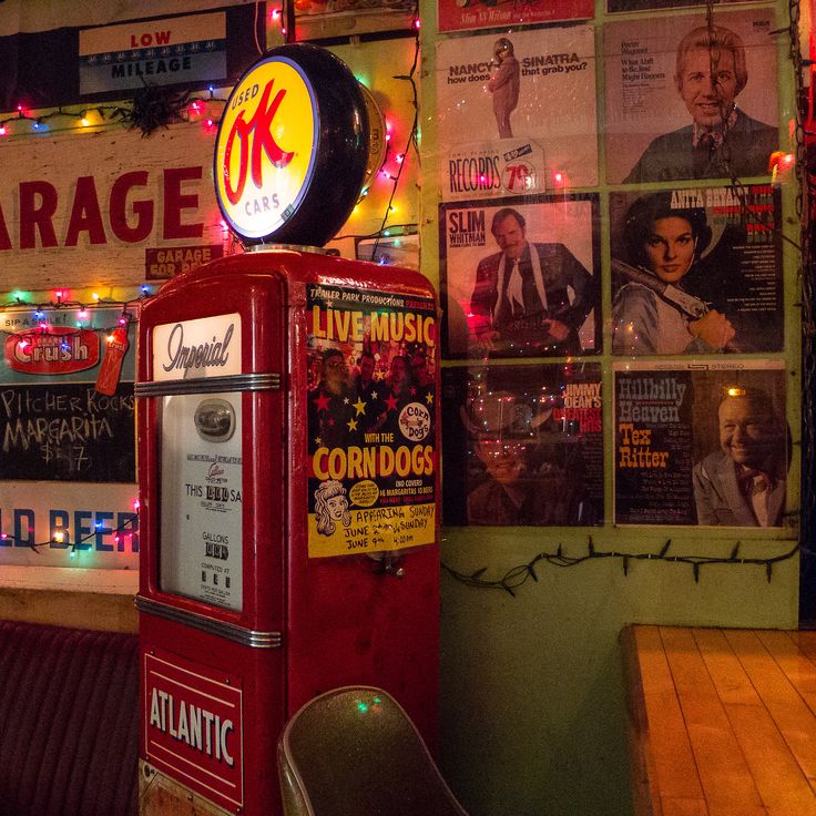 Red vintage gas pump indoors next to retro posters and string lights
