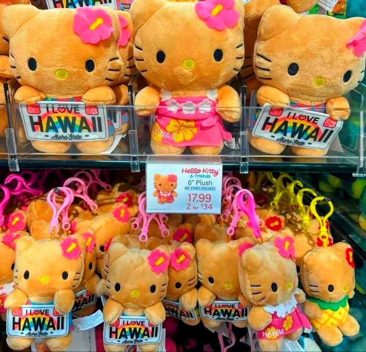 Tan Hello Kitty plush toys in Hawaiian outfits and keychain dolls displayed on a store rack