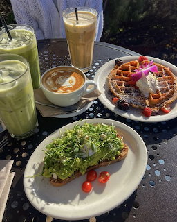 Outdoor table with avocado toast, waffle with berries,iced matcha, iced coffee, and cappuccino
