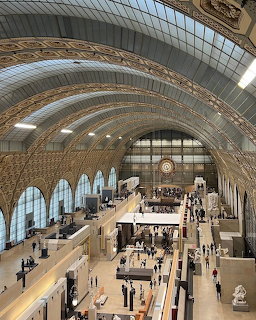 Aerial view inside Musée d'Orsay showing vaulted ceiling, large clock, arched windows, and museum visitors