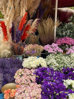 Colorful flower market display with purple, pink, and white bloms alongside dried grasses and feathers