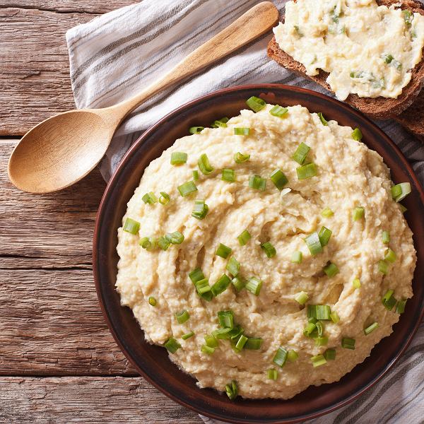 Bowl of creamy egg salad topped with chopped chives, wooden spoon and toast on rustic table