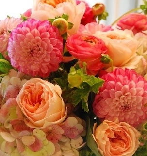 Bouquet of orange, yellow and red flowers with greenery in a clear glass vase.