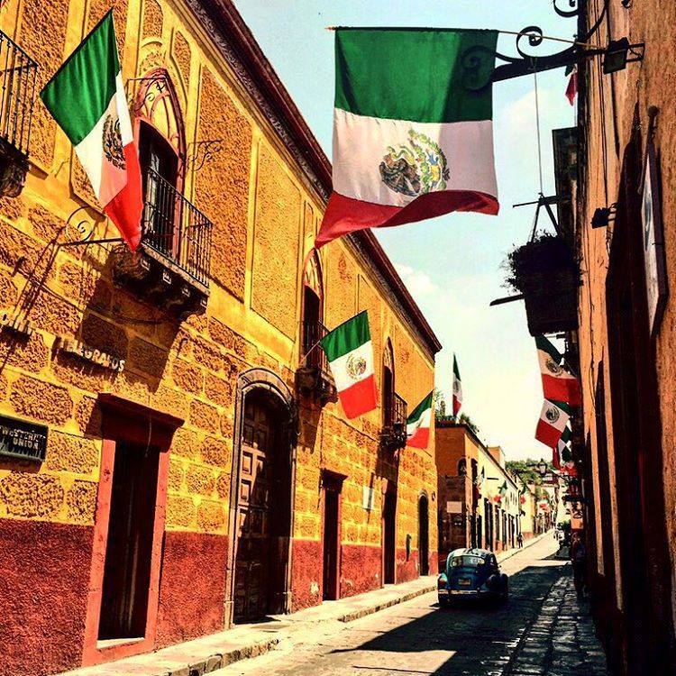 Narrow coblestone street with colonial yellow buildings and Mexican flags in Mexico