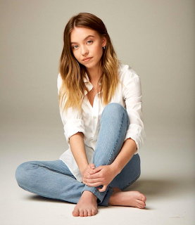 Woman with ombre hair sitting cross-legged in white shirt and light jeans on neutral background