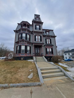Dark ornate Victorian mansion with tower and front staircase under cloudy winter sky