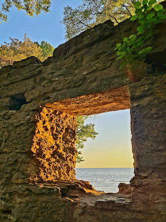 Ocean view through weathered stone arch with sunset sky and foliage