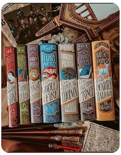 Seven decorative Harry Potter book spines with ornate vintage designs displayed on a wooden shelf