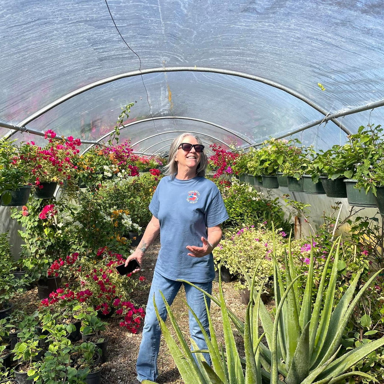 Woman standing in a greenhouse among flowers, hanging plants, and green foliage