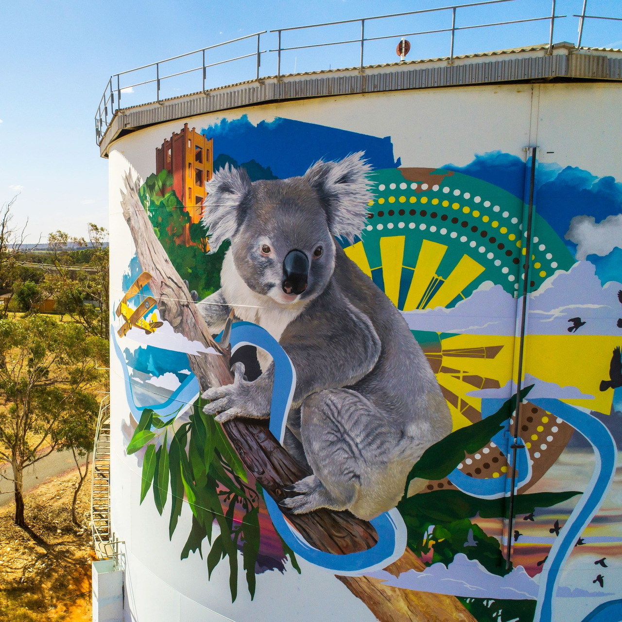 Street art mural of a koala on a water tower with colorful geometric patterns and green leaves