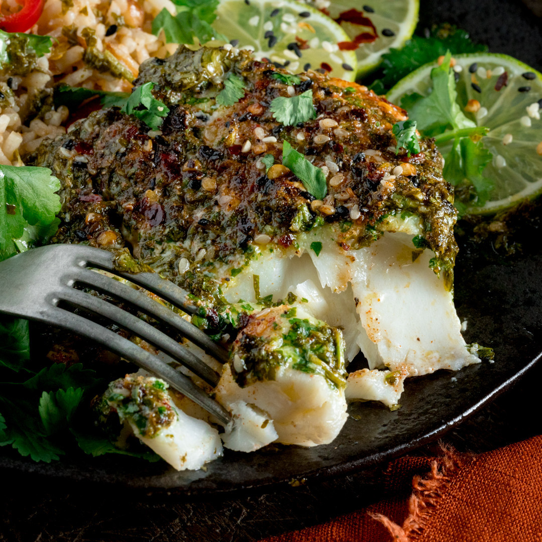 Herb-crusted white fish fillet on a plate with lime slices and greens