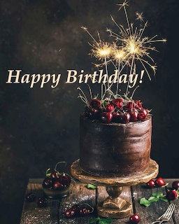 Chocolate birthday cake with cherries, sparklers, and Happy Birthday text on a dark background