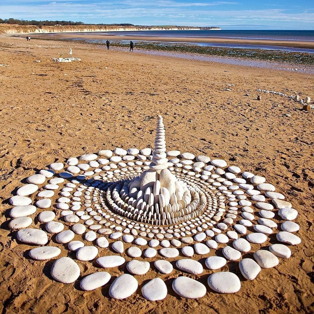 Spiral pattern made from arranged beach stones and pebbles on sandy shore with ocean in background