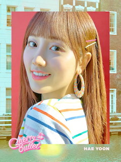 Smiling young woman with long auburn hair, hoop earrings, and a colorful striped top in a pink-framed photo