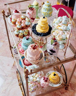 Gold tea cart with assorted colorful desserts, cakes, and treats on two glass shelves