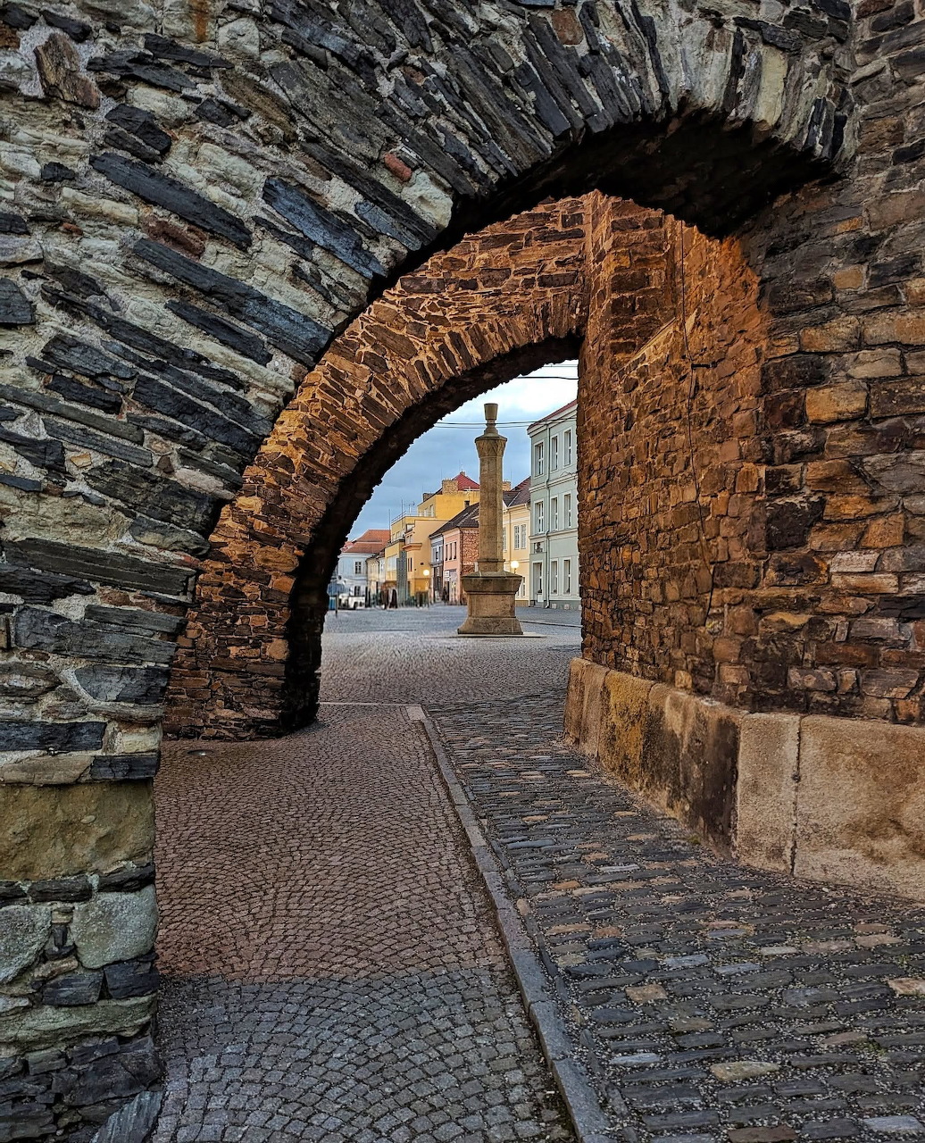 View through an old stone archway to a cobblestone street and historic town square