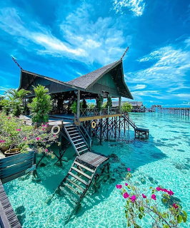 Wooden overwater bungalow with stairs leading into turquoise tropical lagoon under blue sky