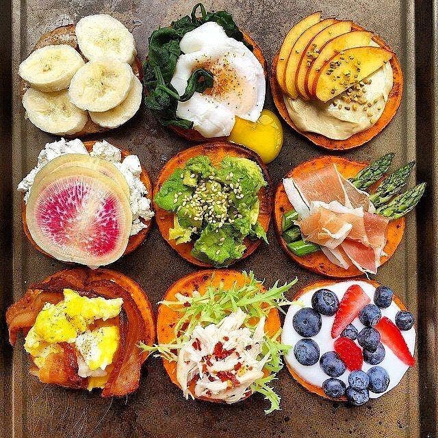 Nine open-faced toasts on a baking tray topped with various colorful ingredients like fruit, avocado, and eggs