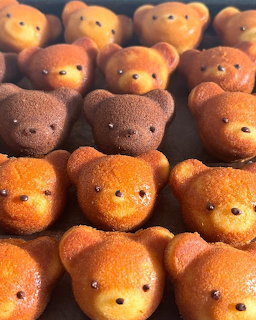 Rows of cute bear-shaped baked pastries in golden and chocolate brown colors on a baking tray