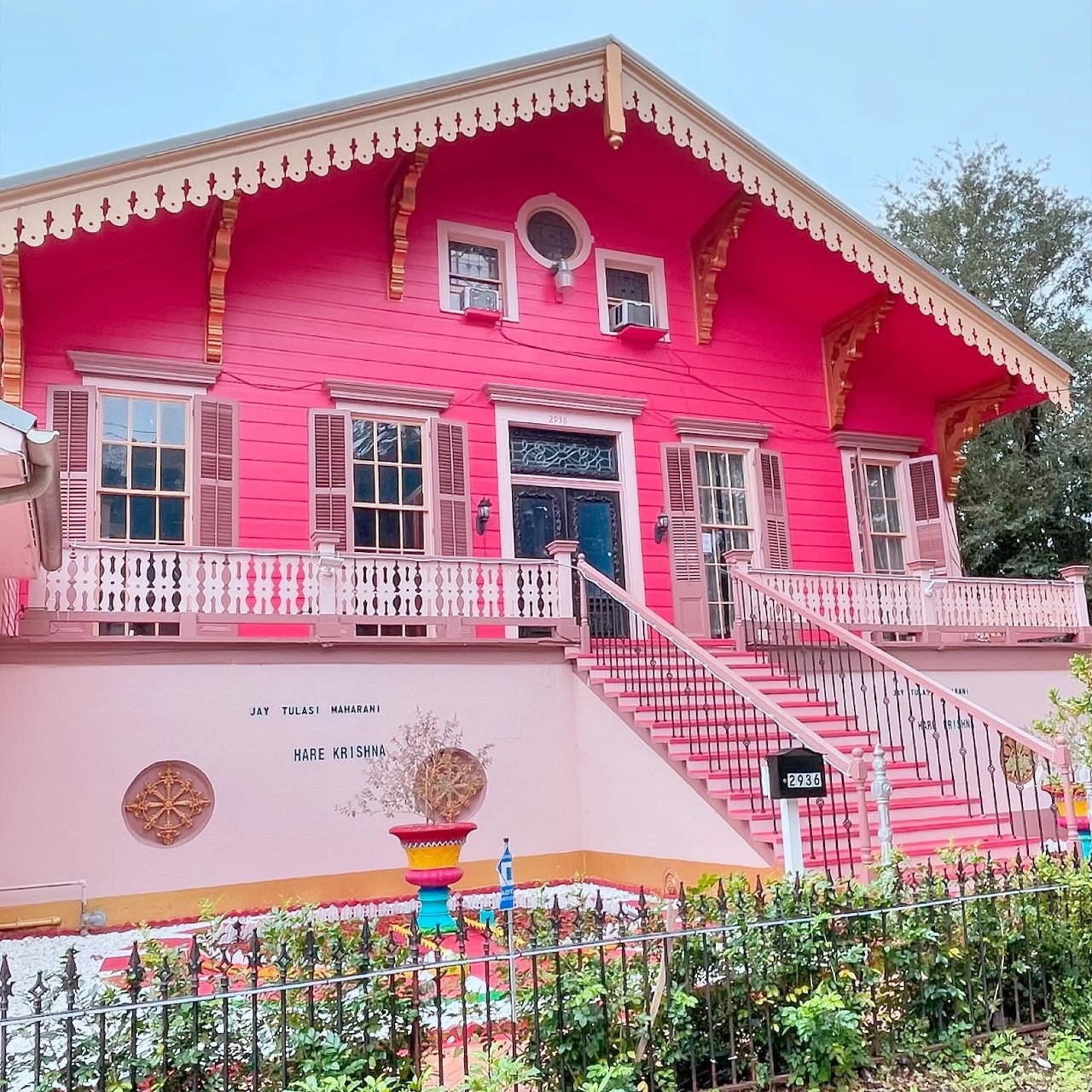 Bright pink Victorian house with white decorative trim, balcony, and twin staircases