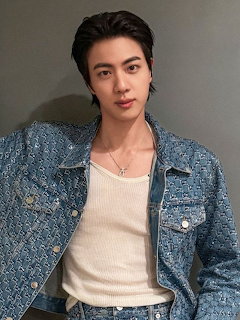 Young man with dark hair wearing a blue denim jacket and white tank top posing indoors