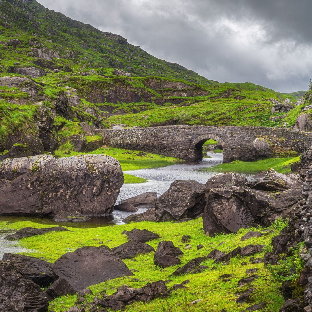 Stone bridge over lush green valley in Co Kerry with mountains and stormy clouds